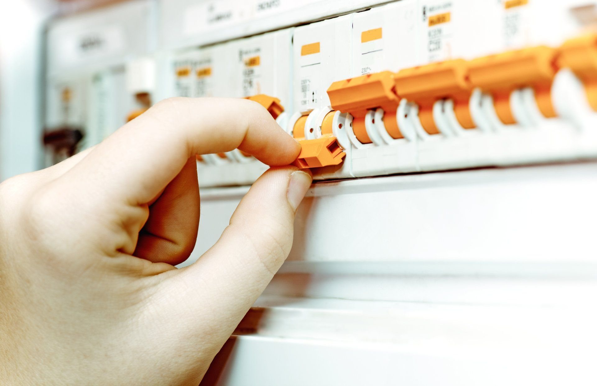 Main actionnant un disjoncteur orange sur un tableau électrique blanc